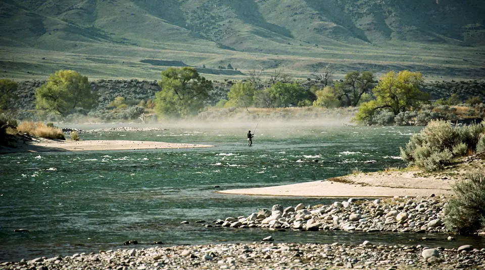 A distant fly angler in a wide clear trout river in a mountain valley