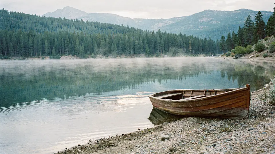 A still mountain lake at first light with a small rowboat on the shore